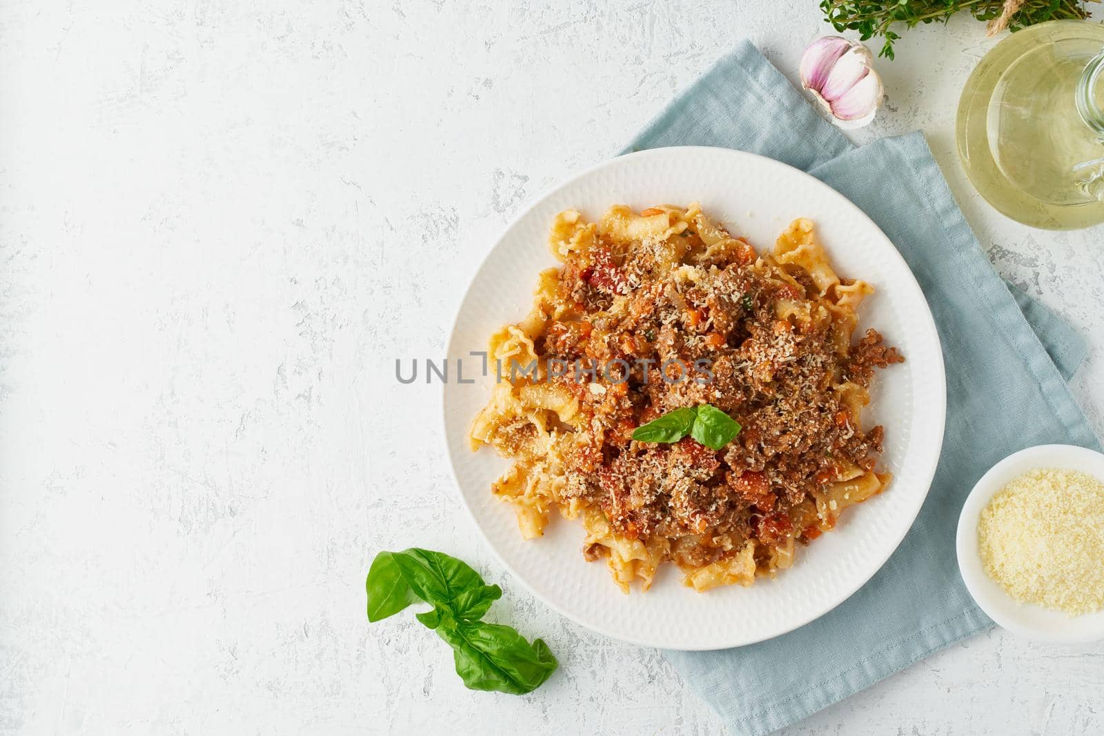 Pasta Bolognese campanelle with mincemeat and tomato sauce, parmesan cheese, basil. Italian dinner, white table. Top view, close up, copy space
