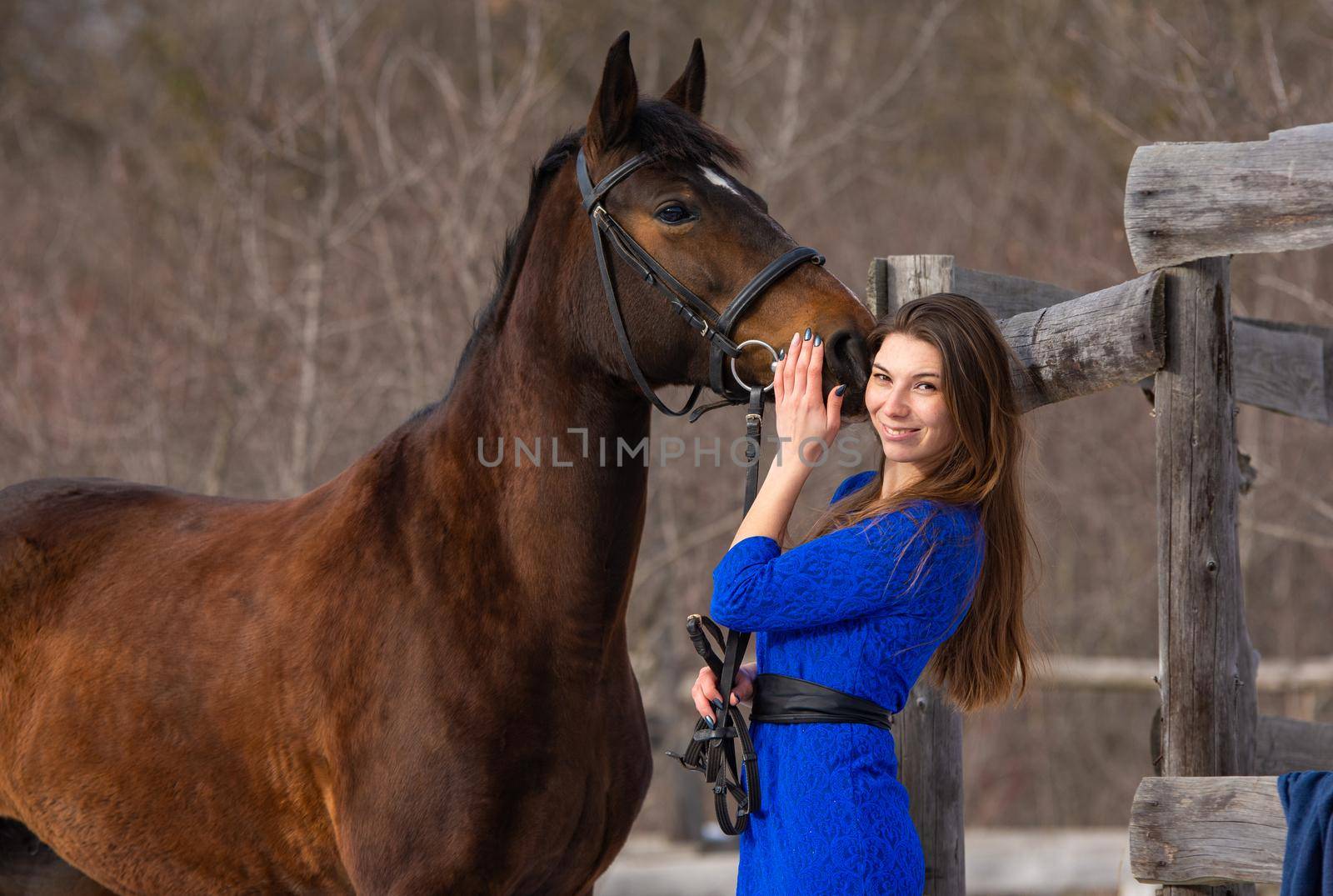 A beautiful girl with a horse is standing near an old wooden fence a