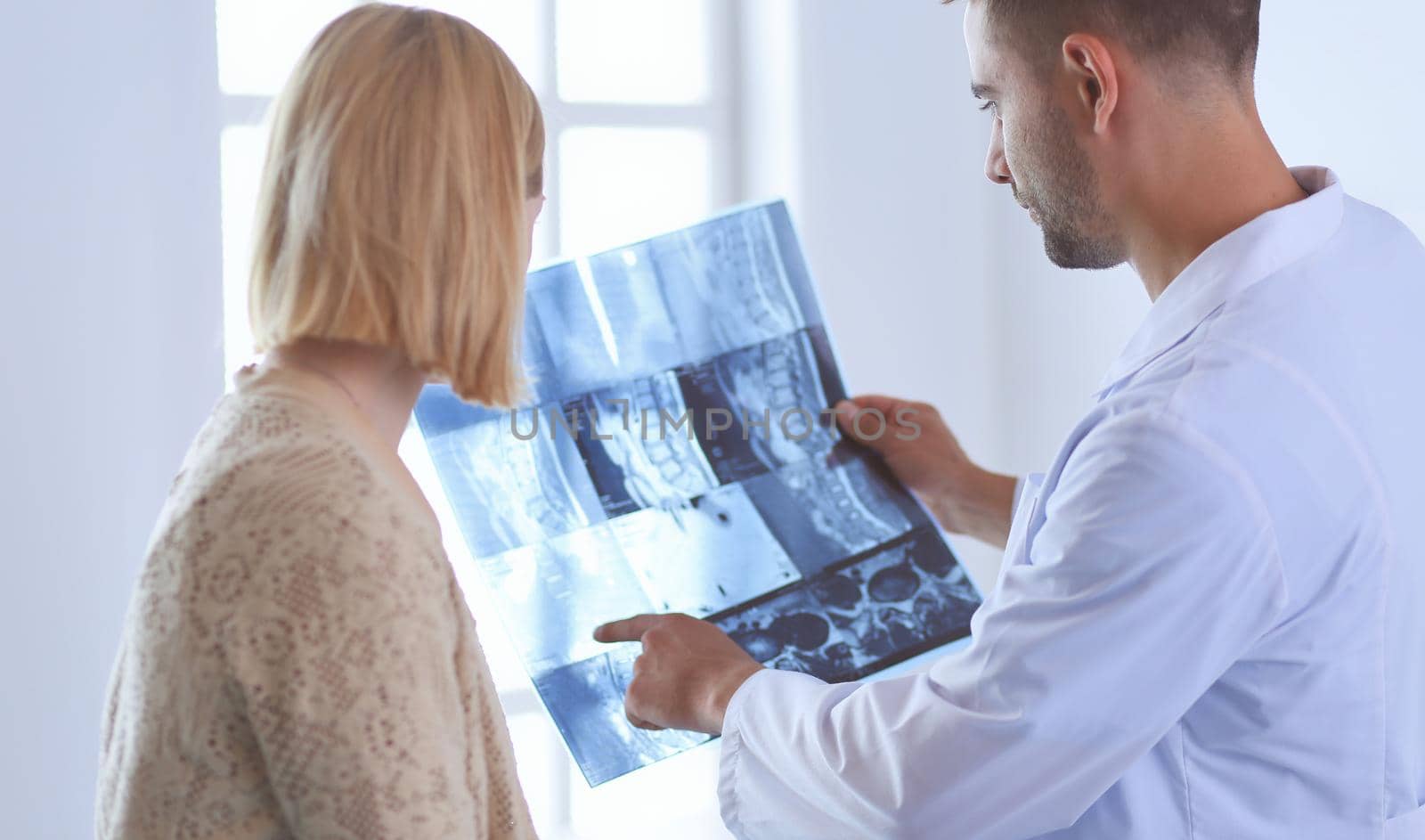 Handsome doctor is talking with young female patient and making notes while sitting in his office