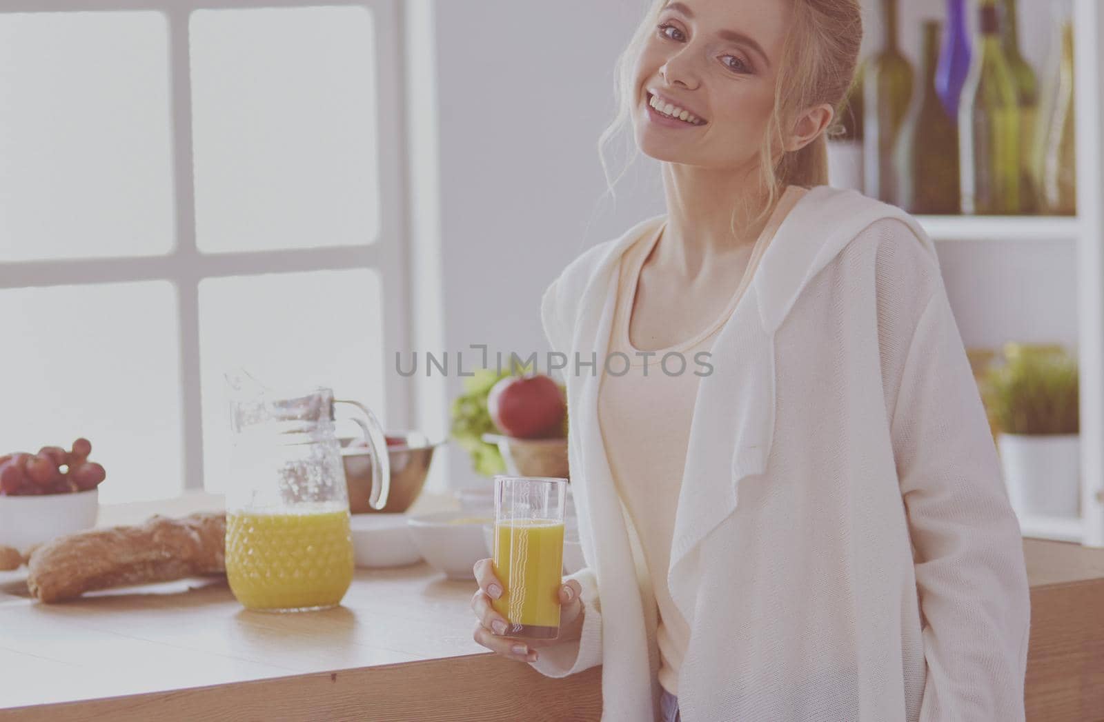 Attractive woman holding a glass of orange juice while standing in the kitchen.