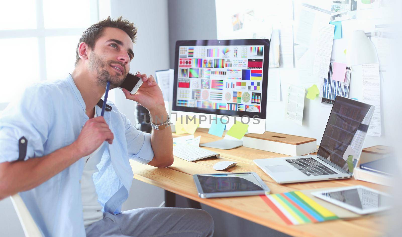 Portrait of young designer sitting at graphic studio in front of laptop and computer while working online