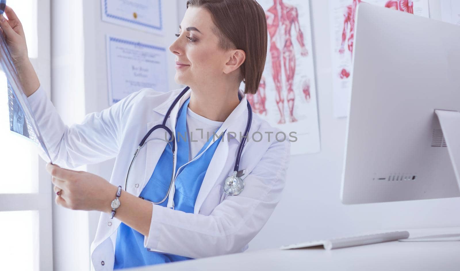 Portrait of doctor sitting in office holding xray image, working on computer.