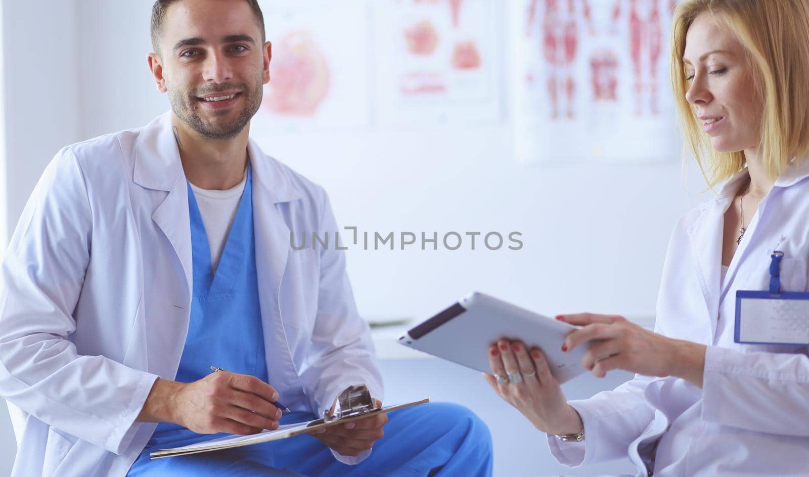 Handsome doctor is talking with young female patient and making notes while sitting in his office.