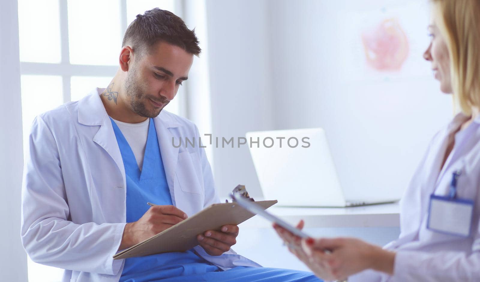 Handsome doctor is talking with young female patient and making notes while sitting in his office.