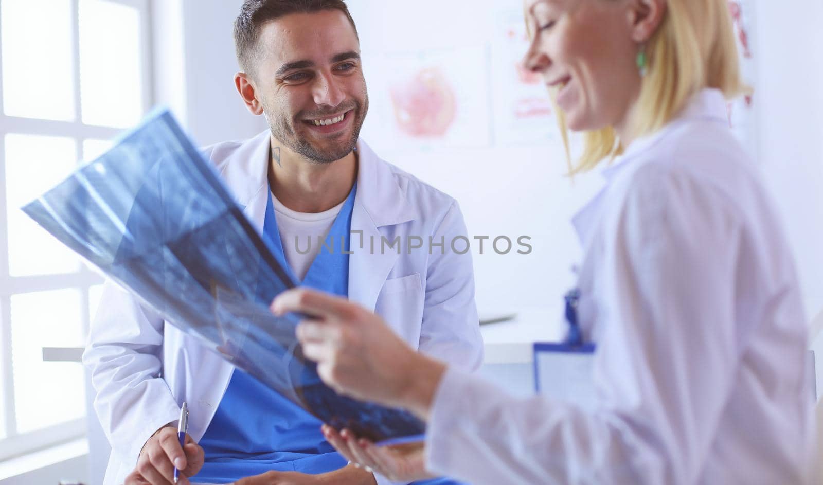 Handsome doctor is talking with young female doctor and making notes while sitting in his office