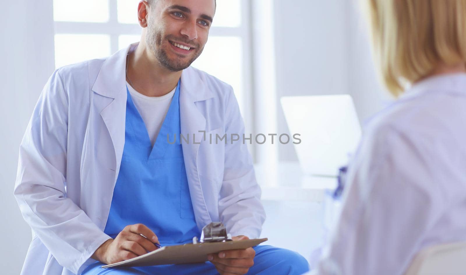 Handsome doctor is talking with young female patient and making notes while sitting in his office.