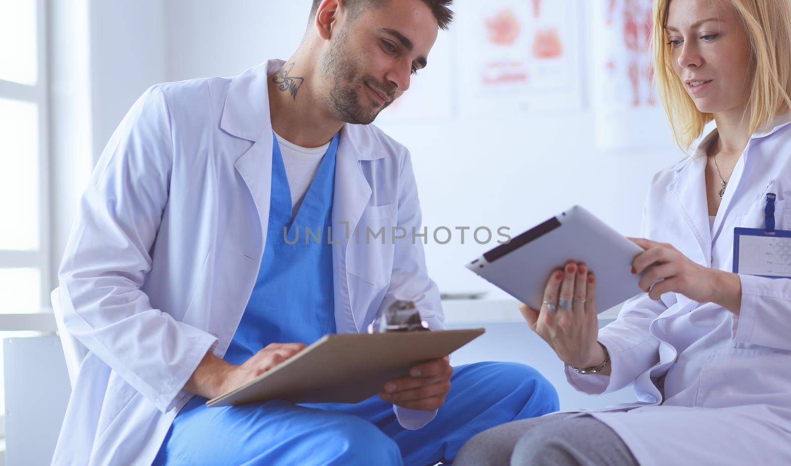 Handsome doctor is talking with young female patient and making notes while sitting in his office.