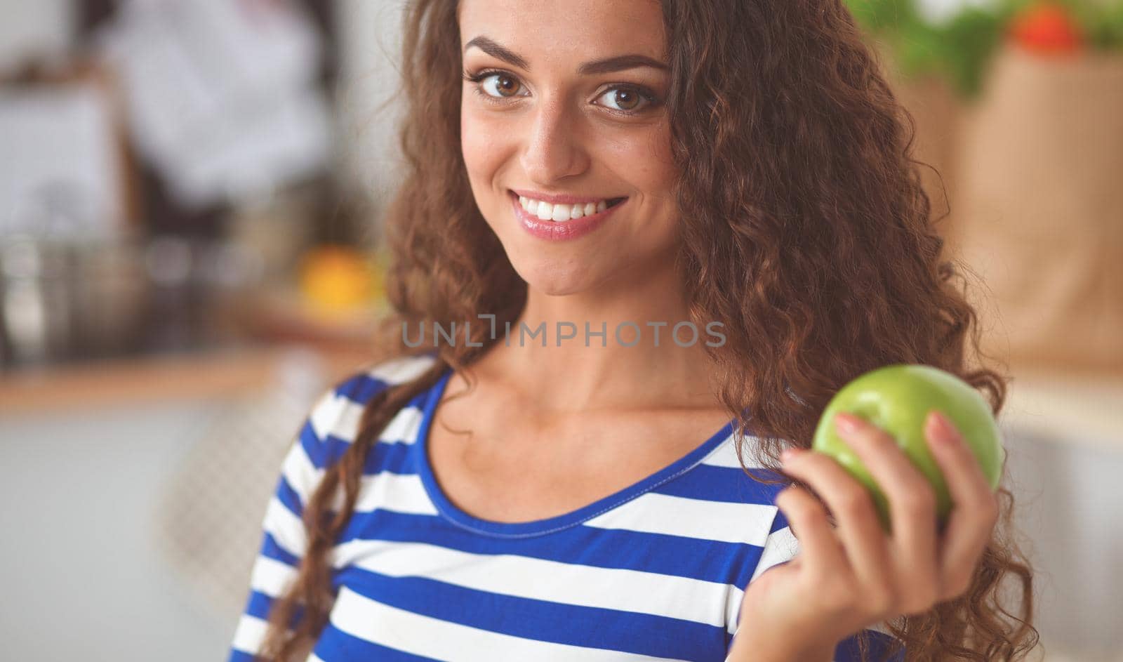 Happy young woman eating apples on kitchen, isolated