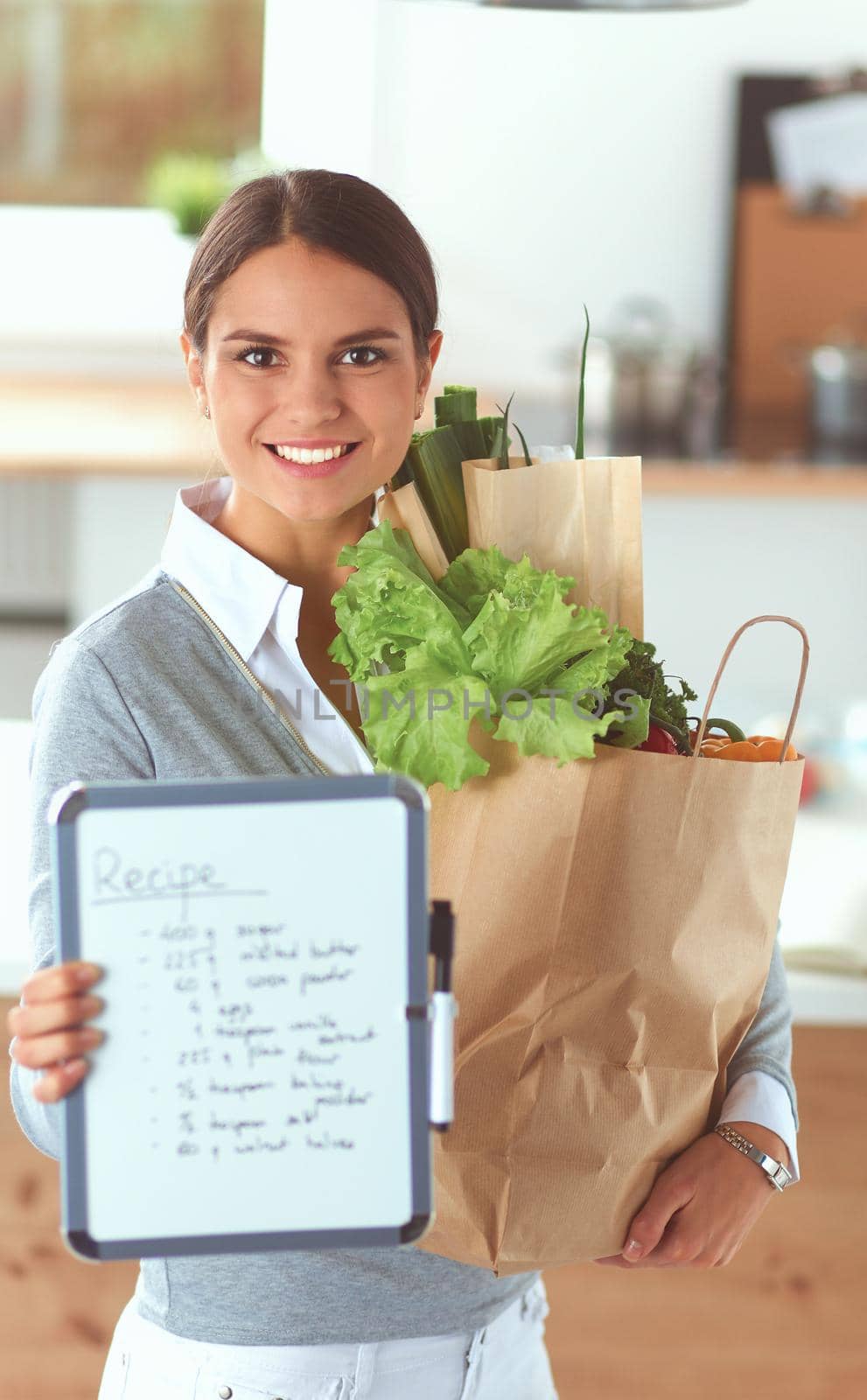 Young woman holding grocery shopping bag with vegetables .Standing in the kitchen.