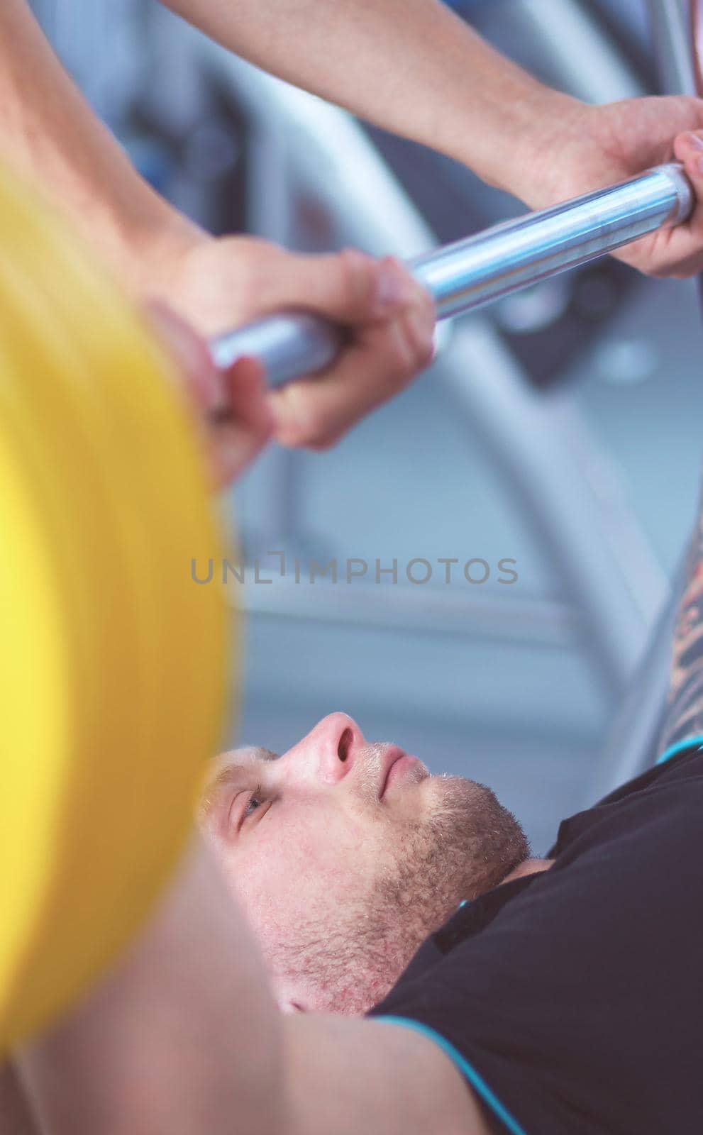 Young man lifting the barbell in the gym with instructor .