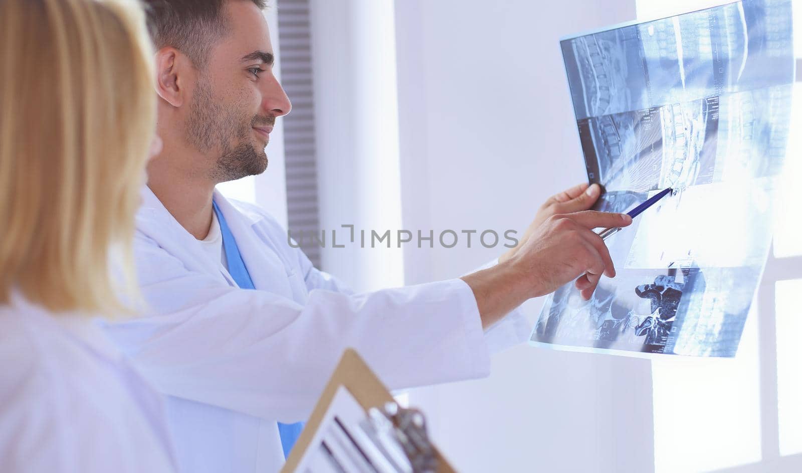 Handsome doctor is talking with young female doctor and making notes while sitting in his office