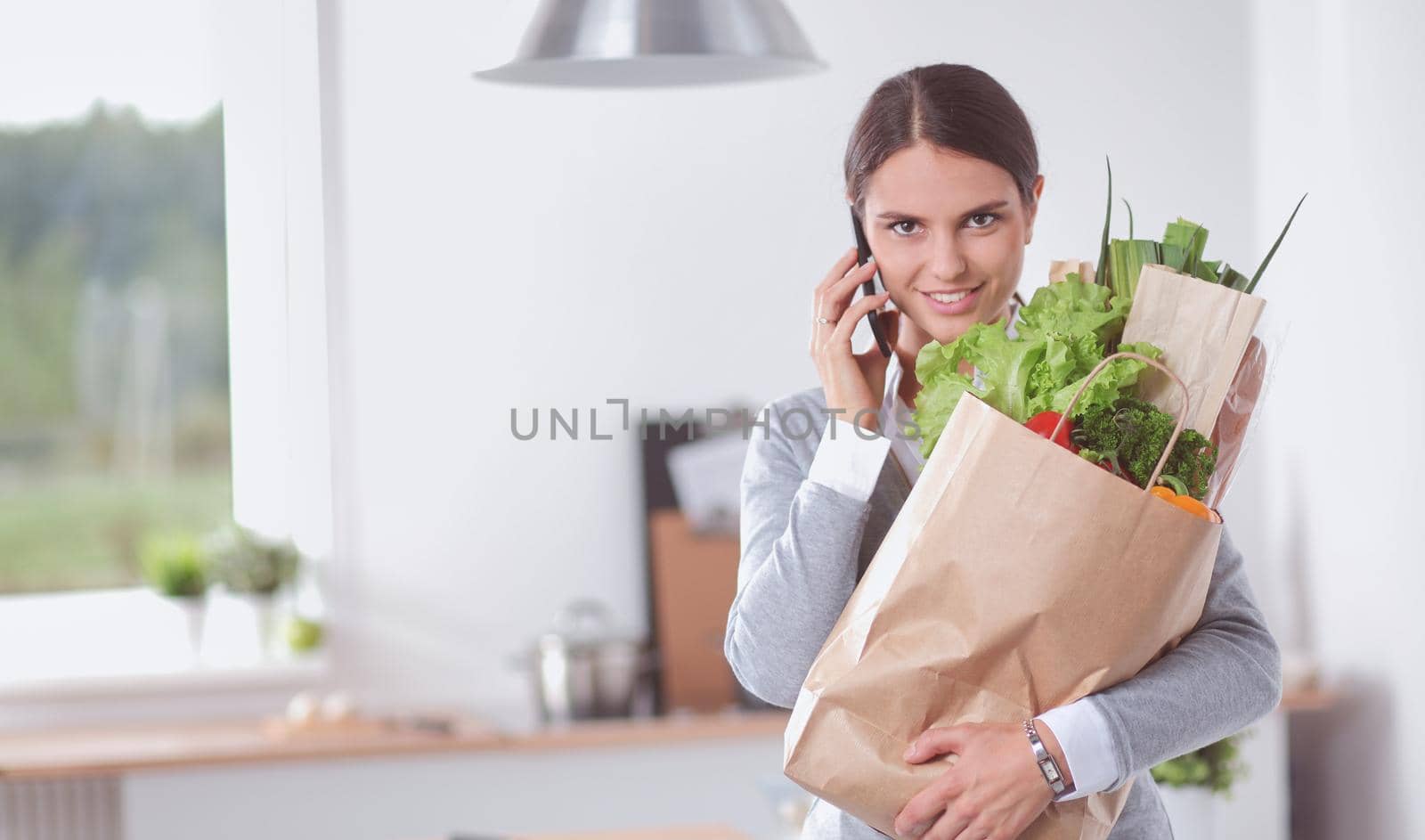 Young woman holding grocery shopping bag with vegetables .Standing in the kitchen.