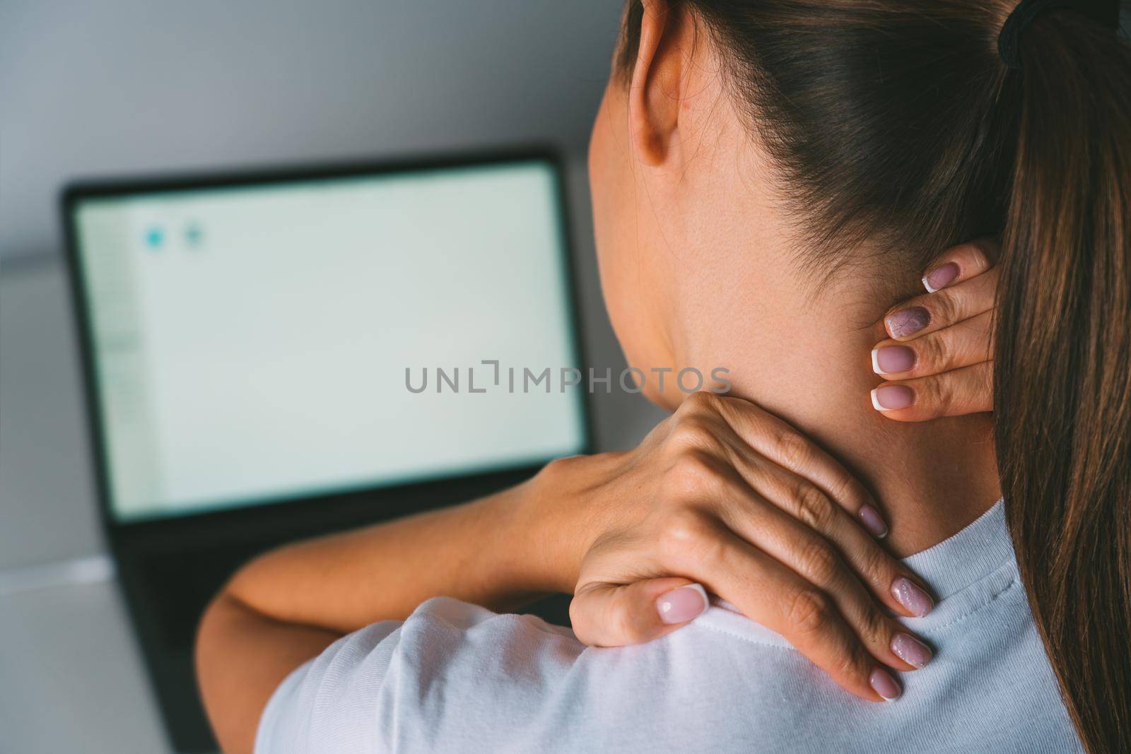 Neck pain after working on laptop or computer. Young woman massaging neck to relieve pain after working on pc. High quality photo