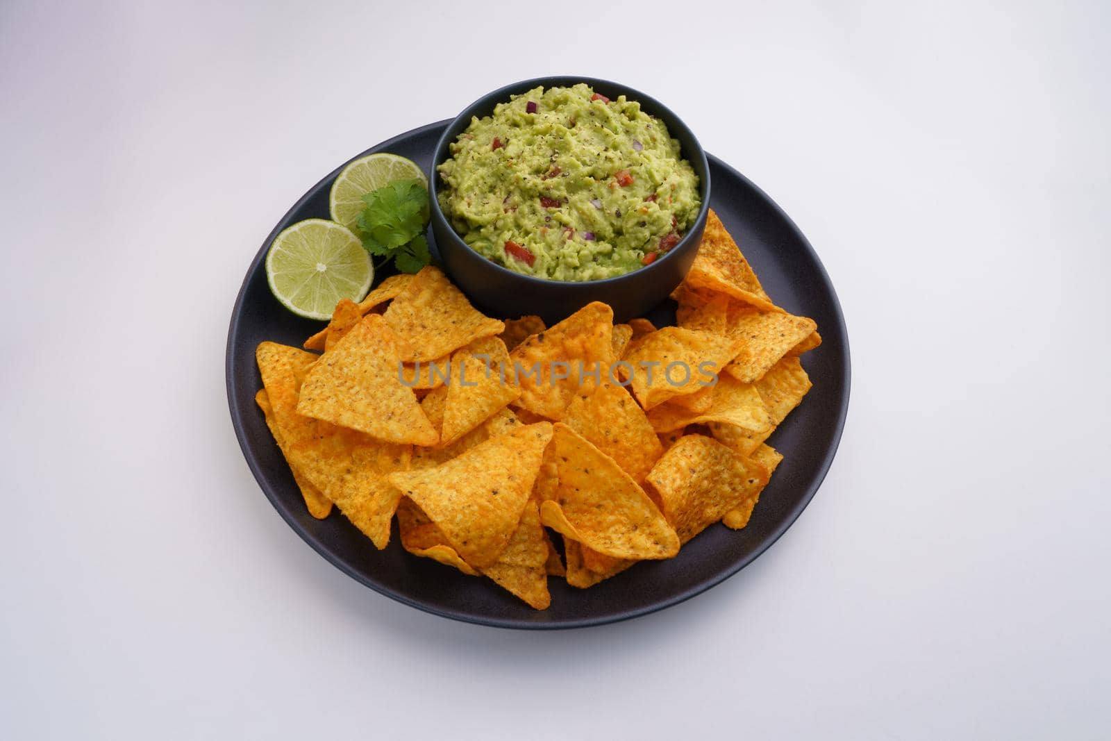 Top view of black plate of guacamole sauce or dip and tortilla chips or nachos isolated on a white background by DariaKulkova
