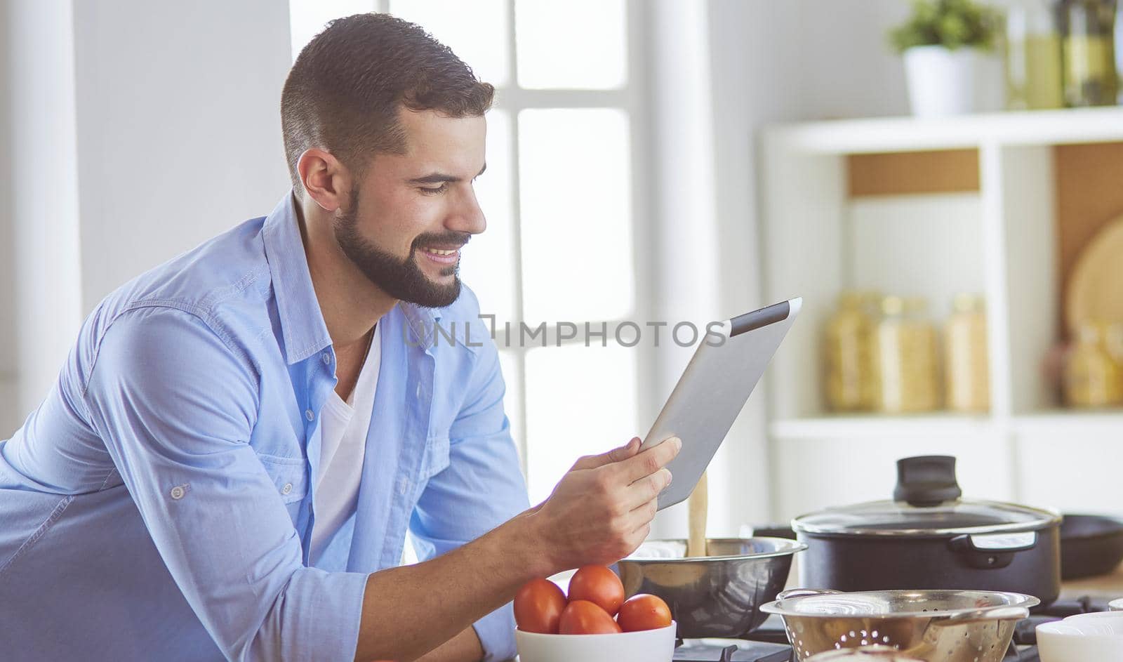 Man following recipe on digital tablet and cooking tasty and healthy food in kitchen at home.