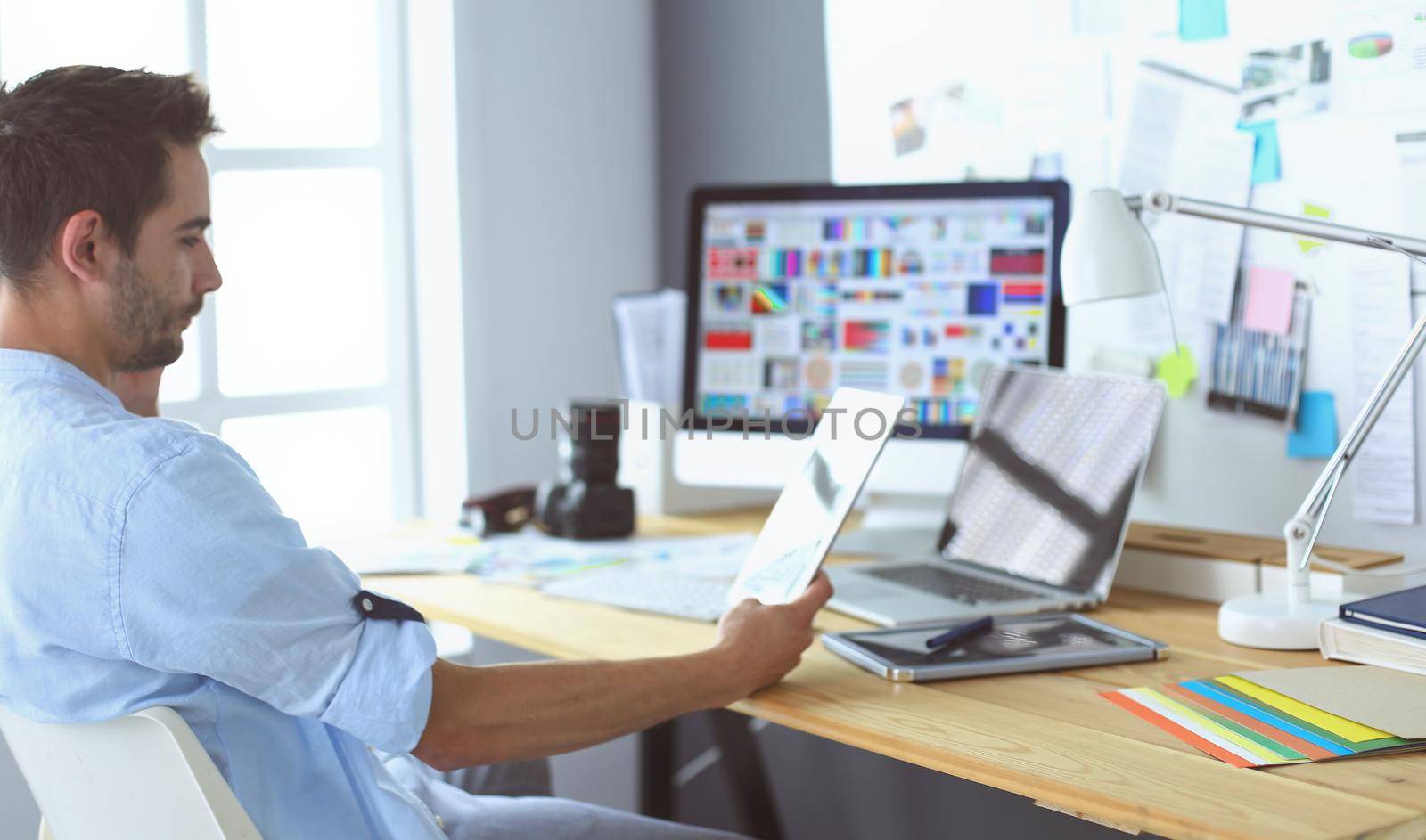 Portrait of young designer sitting at graphic studio in front of laptop and computer while working online