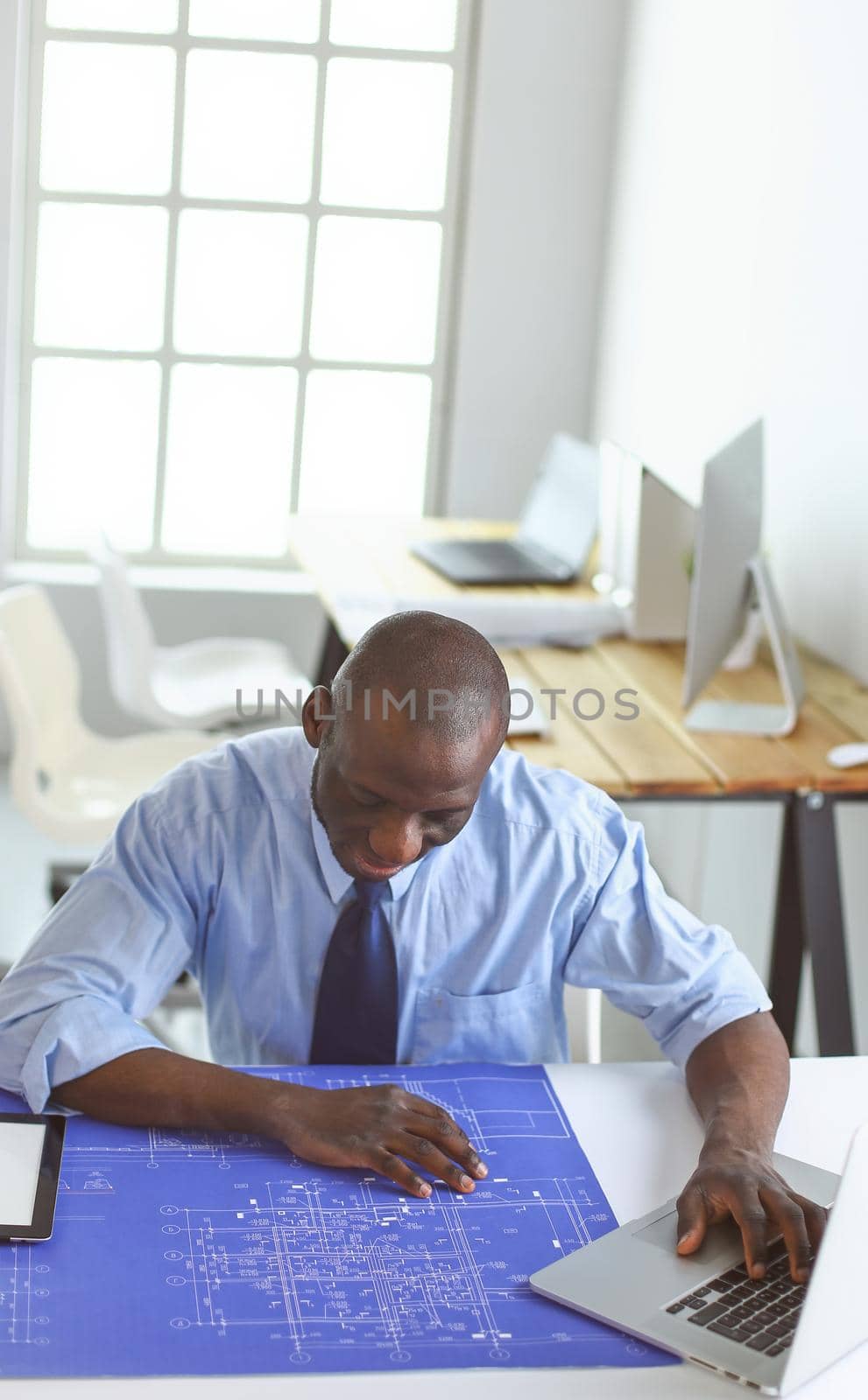 African american architect working with computer and blueprints in office.