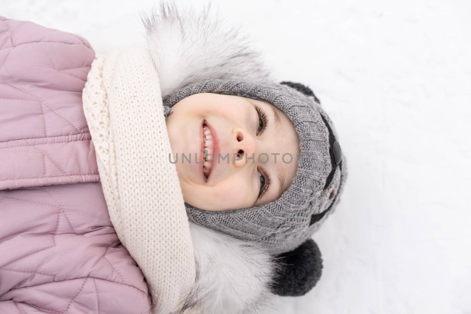 portrait of a happy baby girl lies on the snow and smiles on a winter snowy day