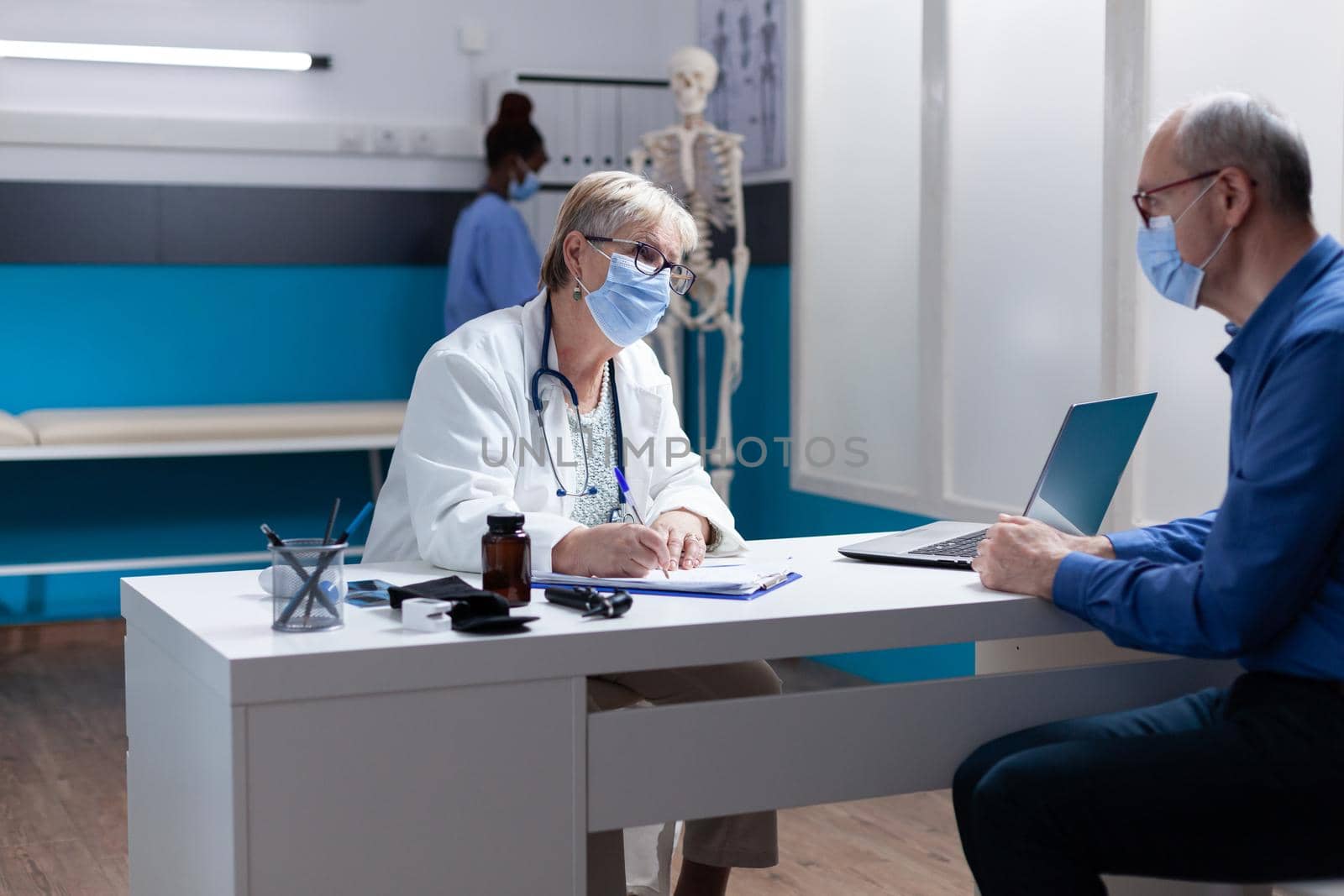 Specialist with face mask signing checkup papers at medical consultation with man. Physician taking notes on clipboard files about healthcare treatment and medicine during pandemic