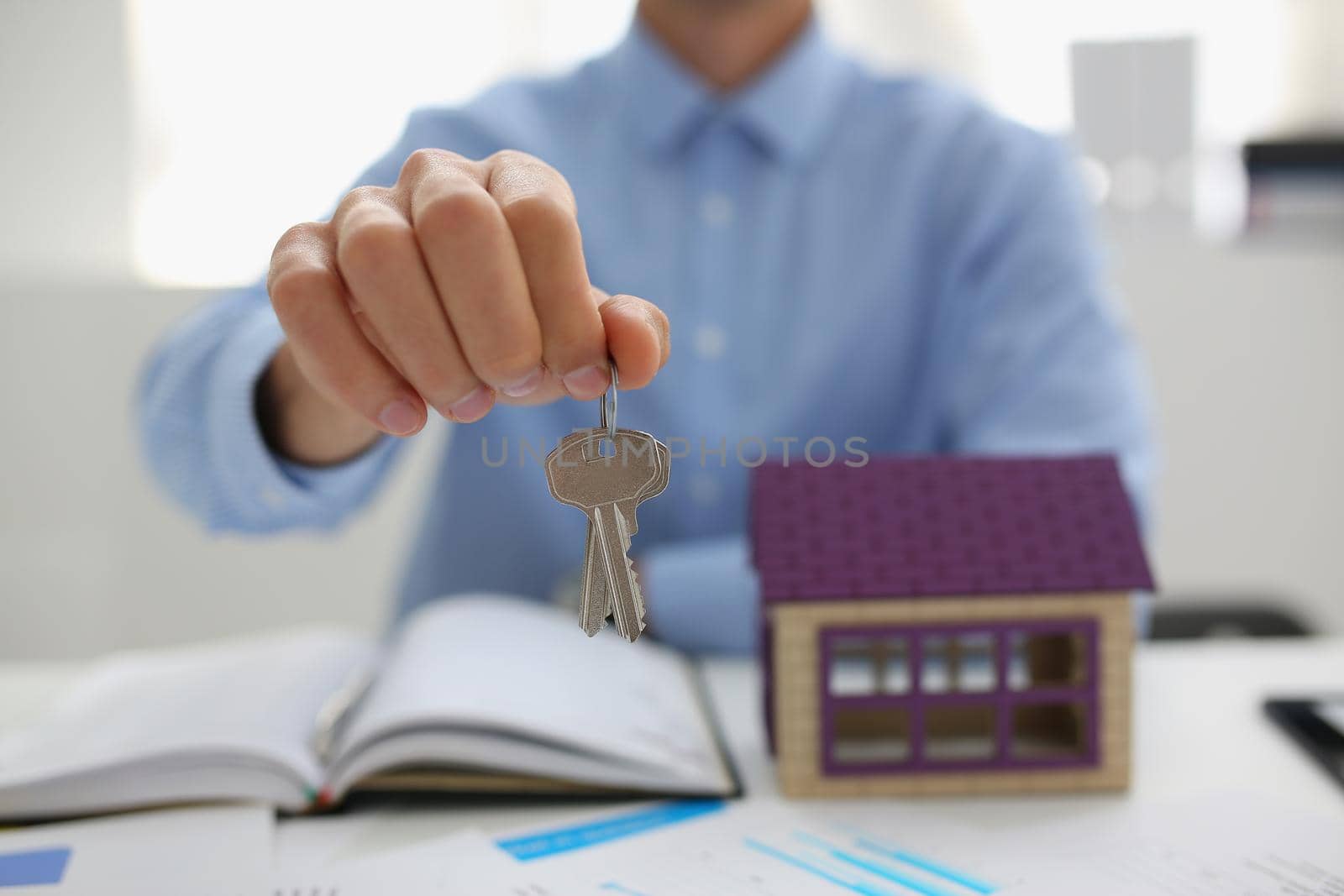 Close-up of male worker in suit give key to unlock new miniature house, buy new accommodation, invest in real estate. Agency, realtor, mortgage concept