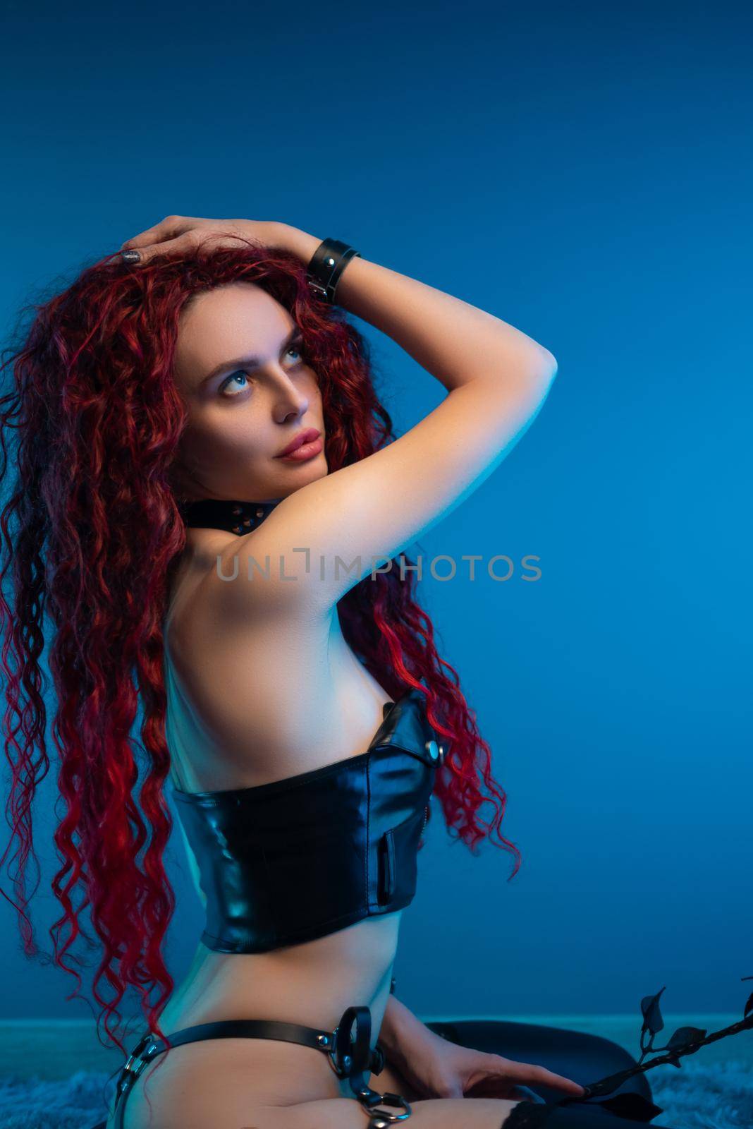 a girl with a chic hairstyle in exciting latex clothes and stockings is sitting on the floor with a leather rose in her hands