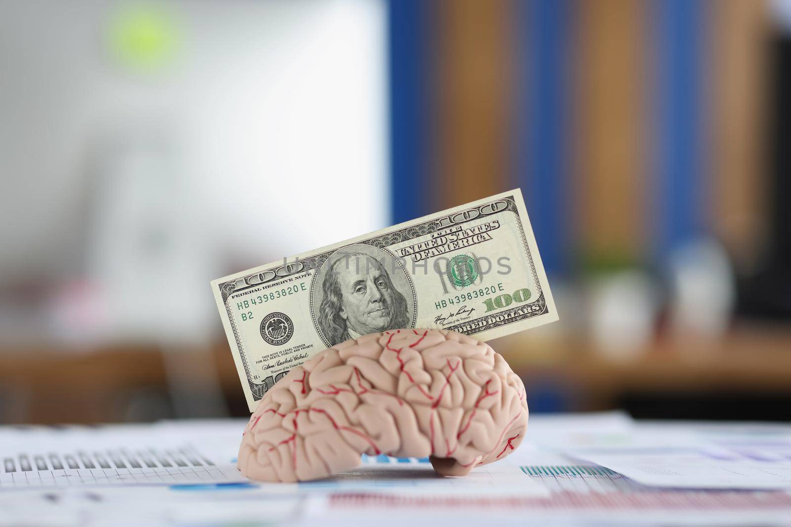 Close-up of banknote put in anatomical model of human brain, mess of business papers on desk. Make money with your intellect. Earn money, use brain concept