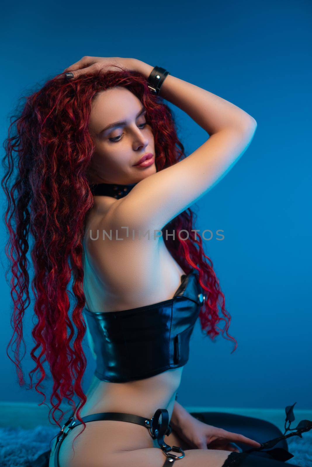 a girl with a chic hairstyle in exciting latex clothes and stockings is sitting on the floor with a leather rose in her hands