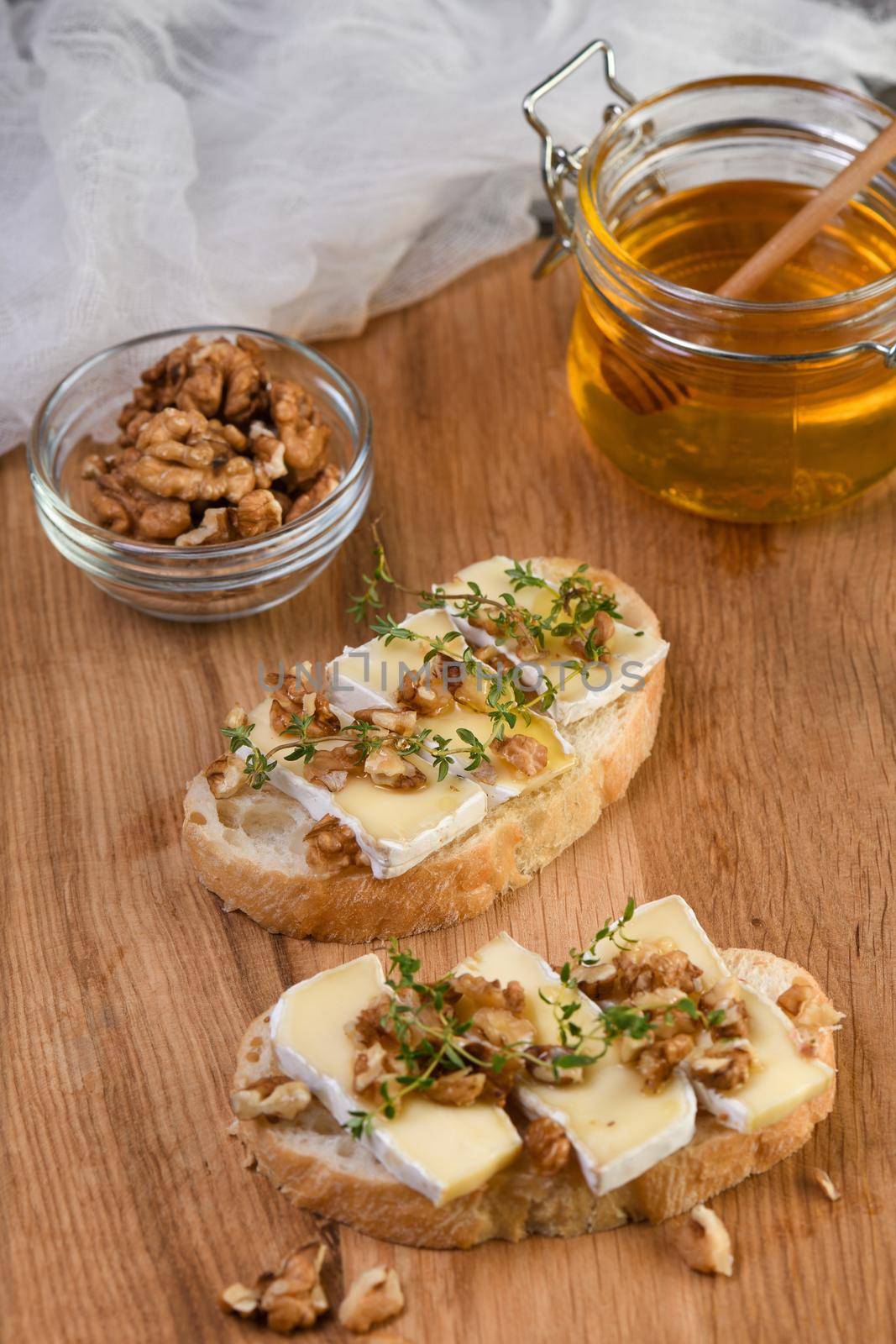 Open sandwiches with soft brie cheese and thyme, honey and nuts on a wooden board