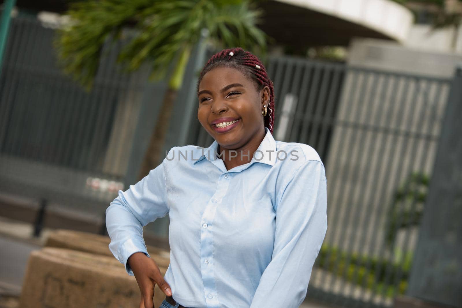 African girl standing in blue shirt looking at camera laughing.