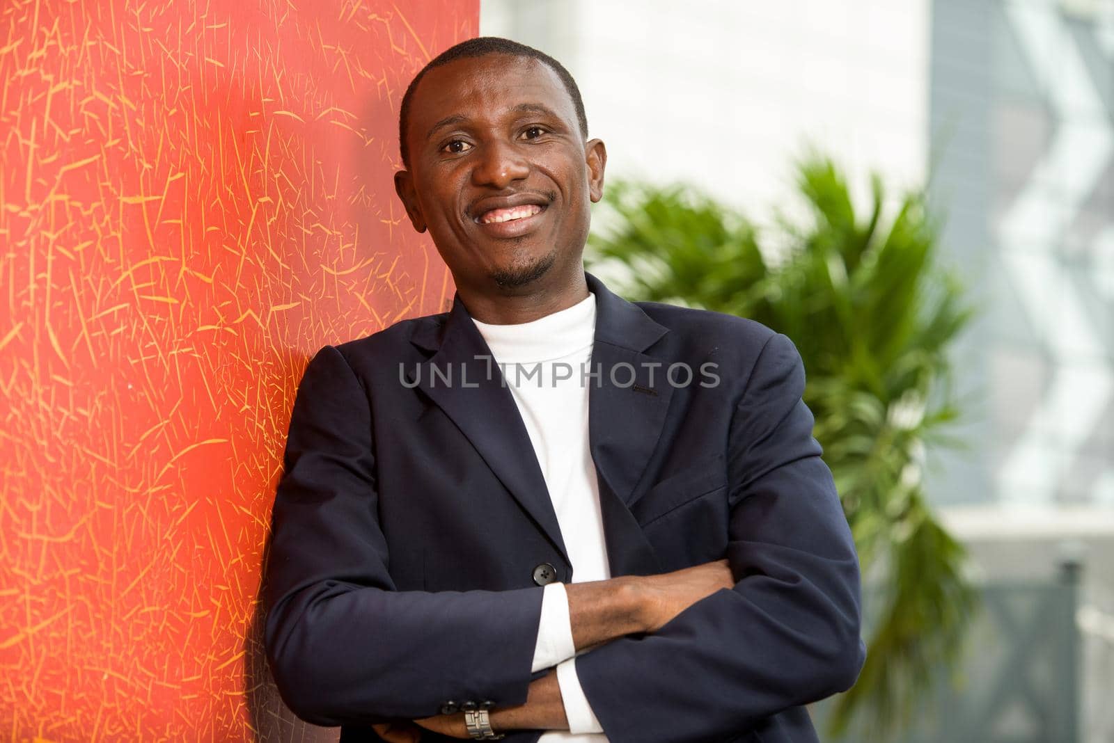 young african man standing in arms crossed suit looking at camera smiling.