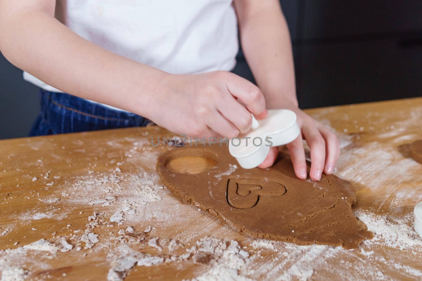 A little girl makes heart-shaped cookies from rye dough. The concept of Valentine's Day and healthy baking. Cooking cookies in close-up.