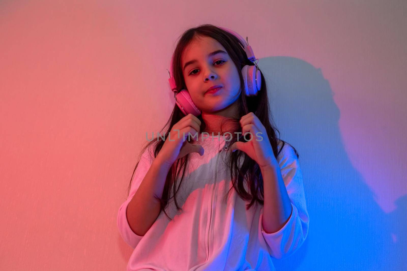 Little girl in pink headphones dancing to music in neon pink blue light