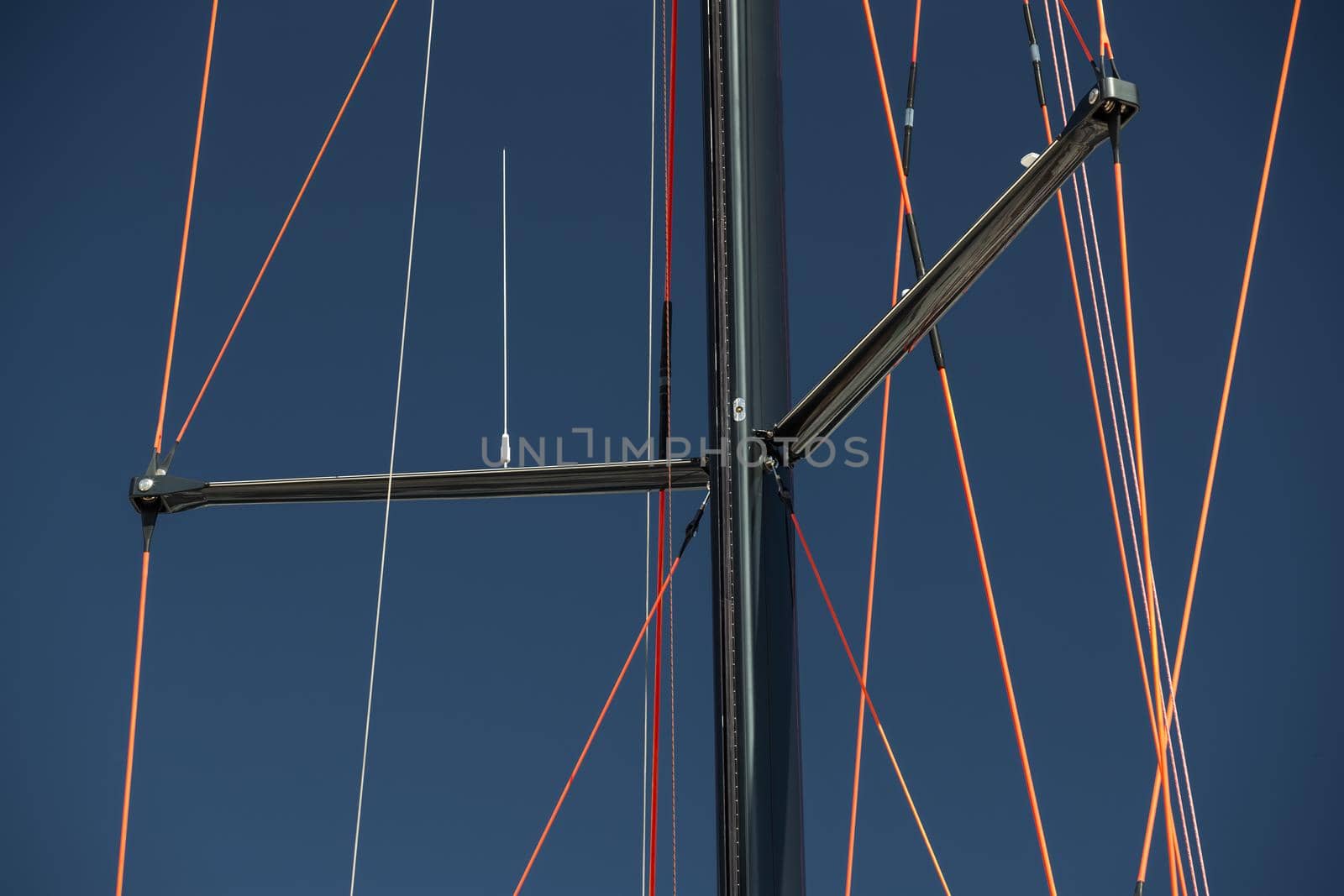 Close up view of the mast of huge sailboat at clear weather, blue sky on a background, ropes by red color. High quality photo
