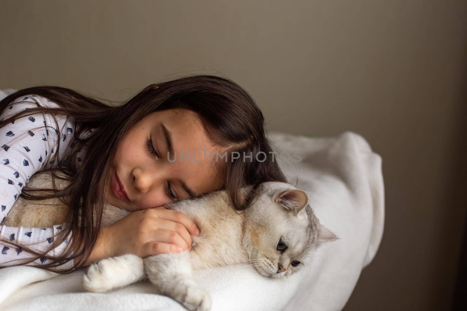 The little girl lies , sleep with a white cat on the bed, hugs him, closes her eyes. Copy space