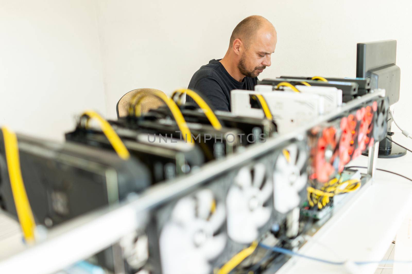 Young programmer adjusting cryptocurrency mining rig to optimal operational settings. High quality photo