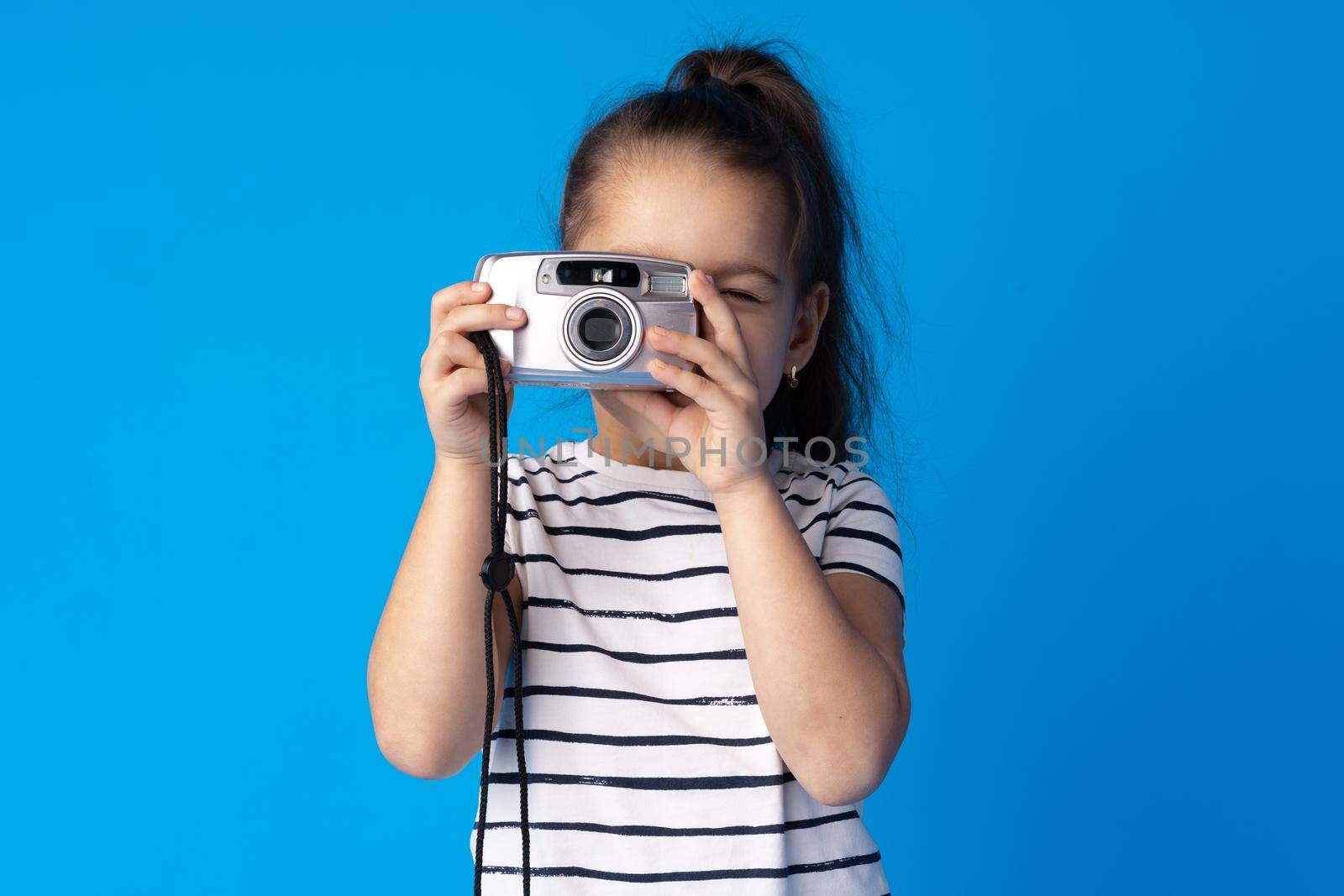 Portrait of a little girl with camera against blue background by Fabrikasimf