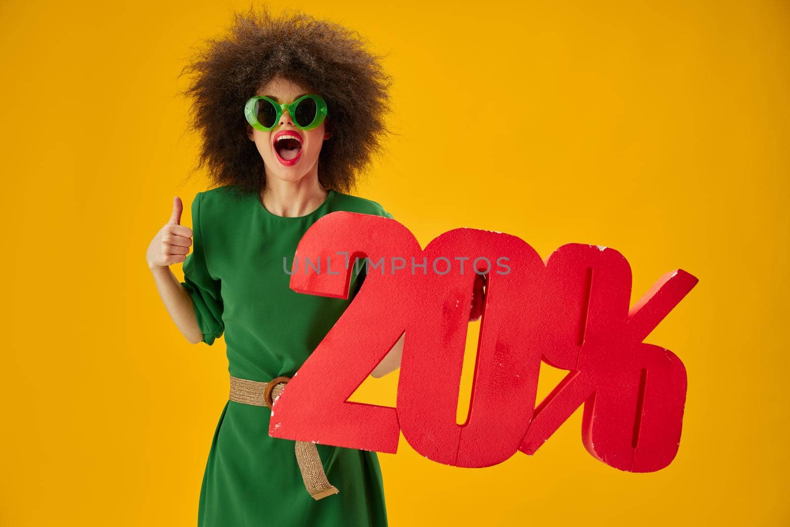 Portrait of a charming lady green dress afro hairstyle dark glasses twenty percent in hands color background unaltered. High quality photo