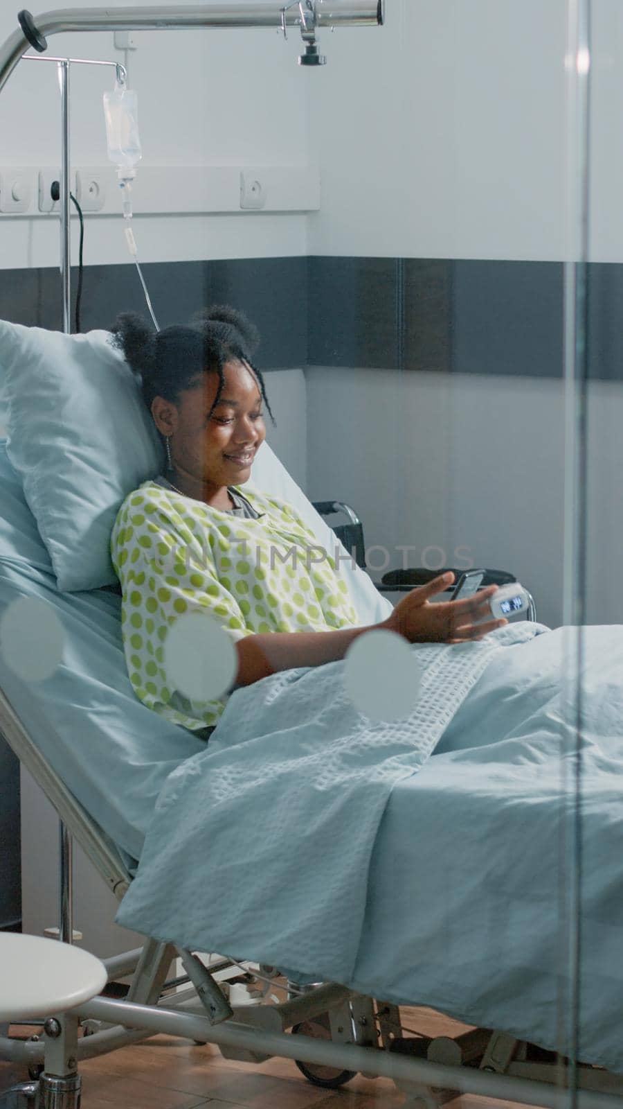 Ill patient holding mobile phone to talk on video call communication with friends. Woman with disease using online video conference to have conversation with family in hospital ward.