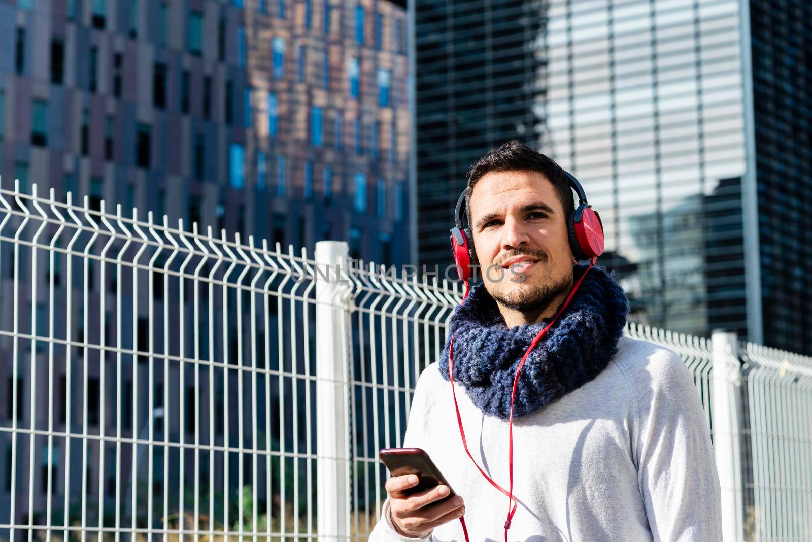 Young man listening music by headphones while holding a mobile phone outdoor by raferto1973