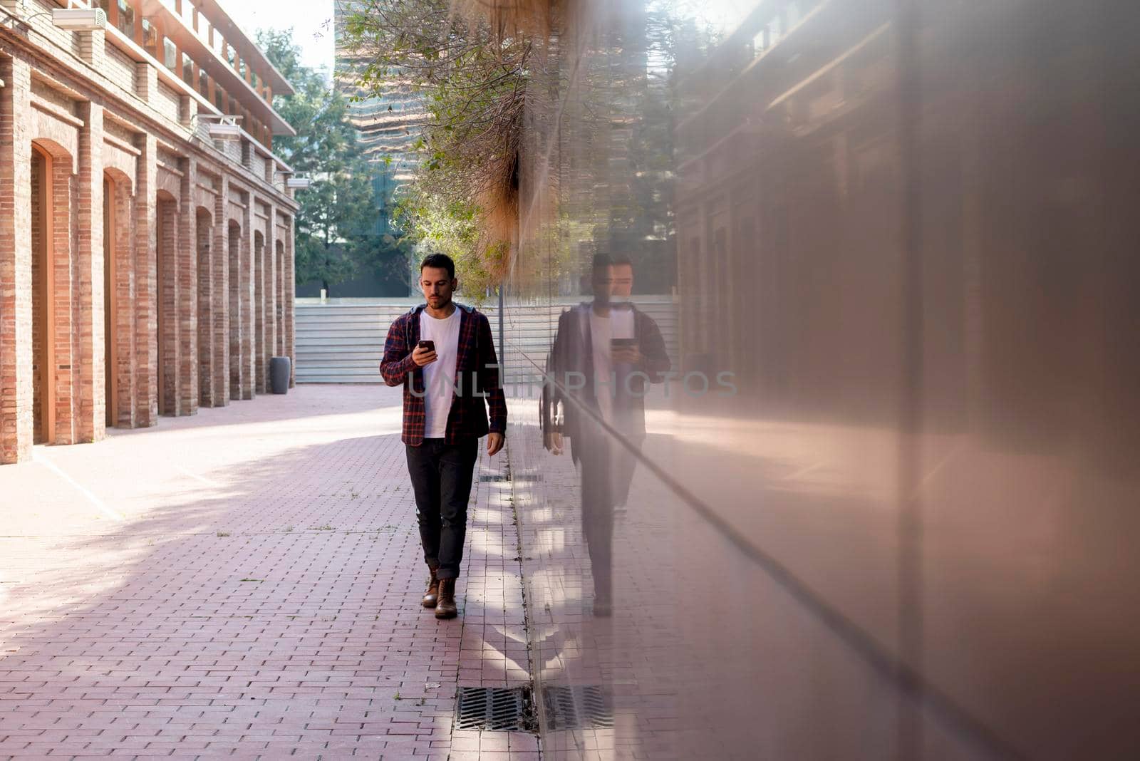 Young man walking while using smartphone outdoors