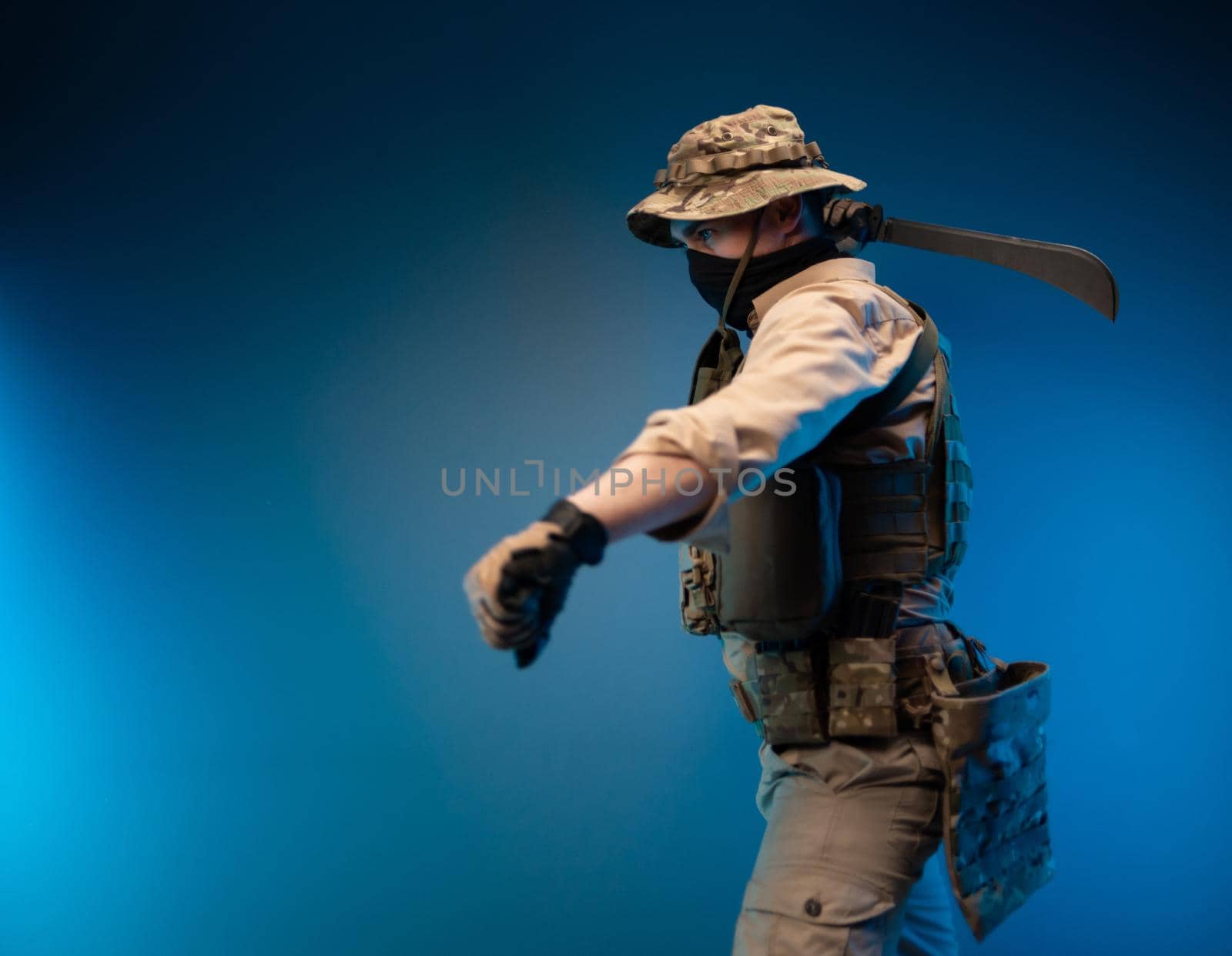 an army soldier in military clothes swings to strike with a machete in his hand