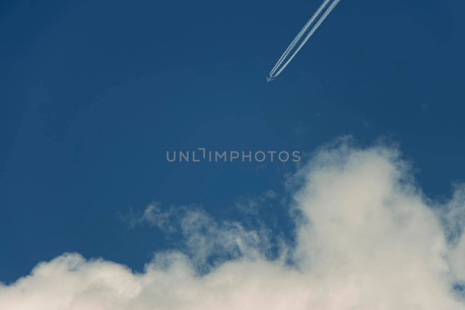 Plane with contrail flying towards fluffy cumulus cloud in blue sky by StefanMal