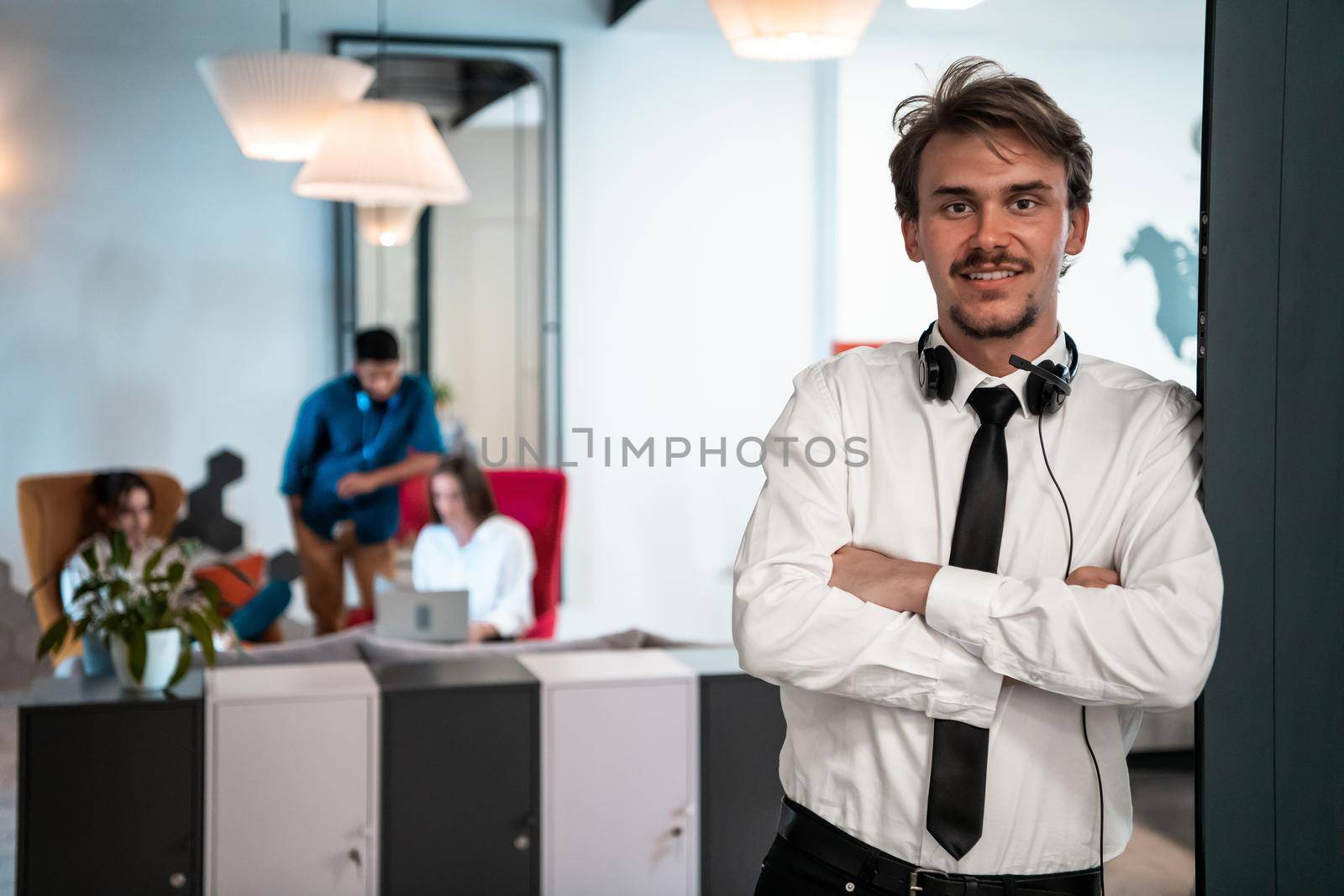 Portrait of successful businessman entrepreneur with headphones around his neck and colleagues in the background at busy startup office. High-quality photo