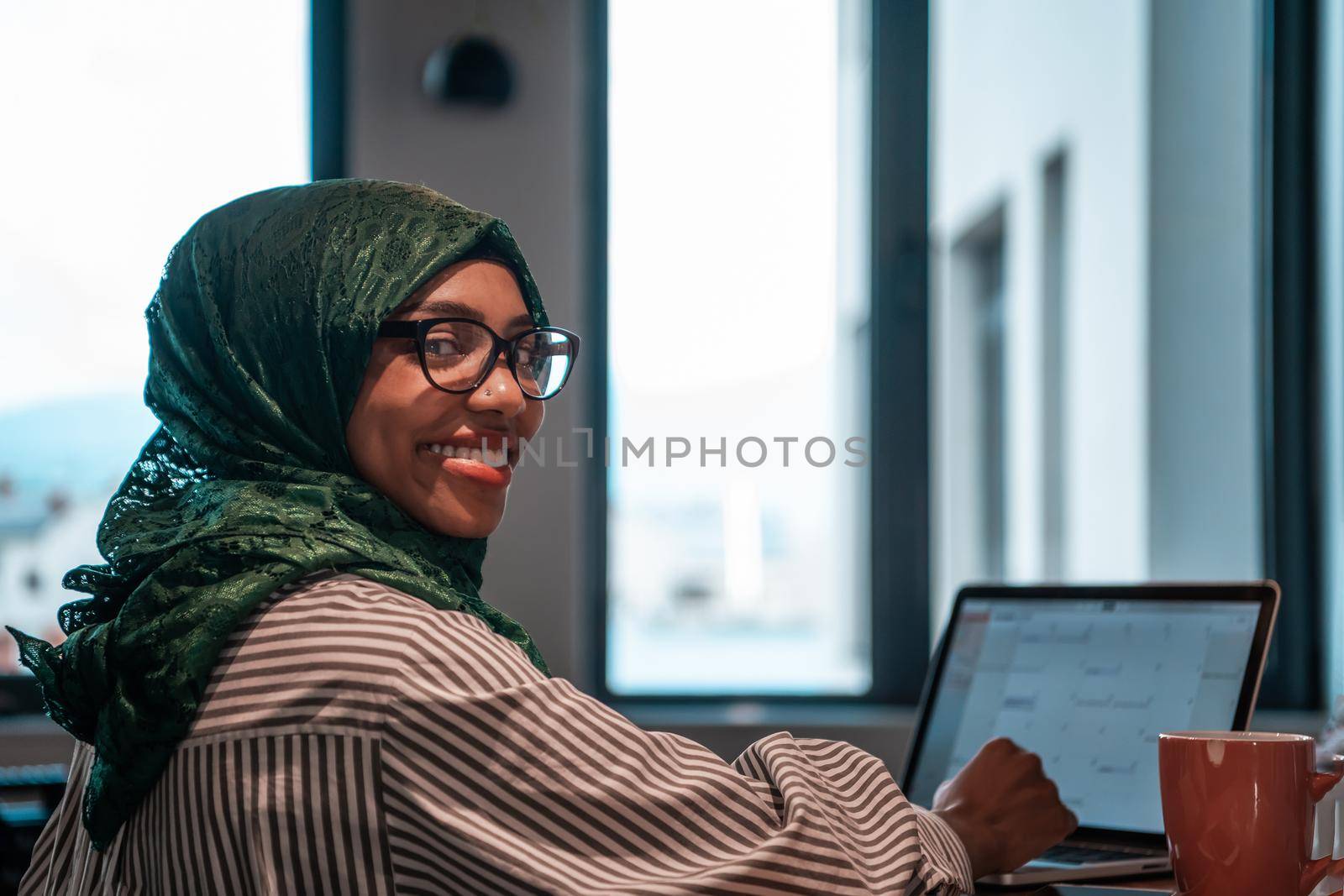 Business woman wearing a green hijab using laptop in relaxation area at modern open plan startup office. Selective focus by dotshock