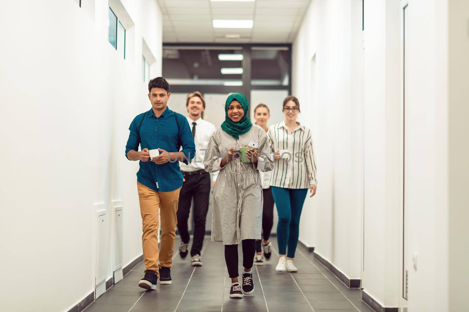 Multi-ethnic startup business team walking through the hallway of the building while coming back from a coffee break by dotshock