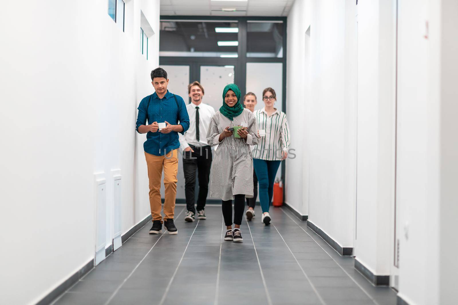 Multi-ethnic startup business team walking through the hallway of the building while coming back from a coffee break. High-quality photo