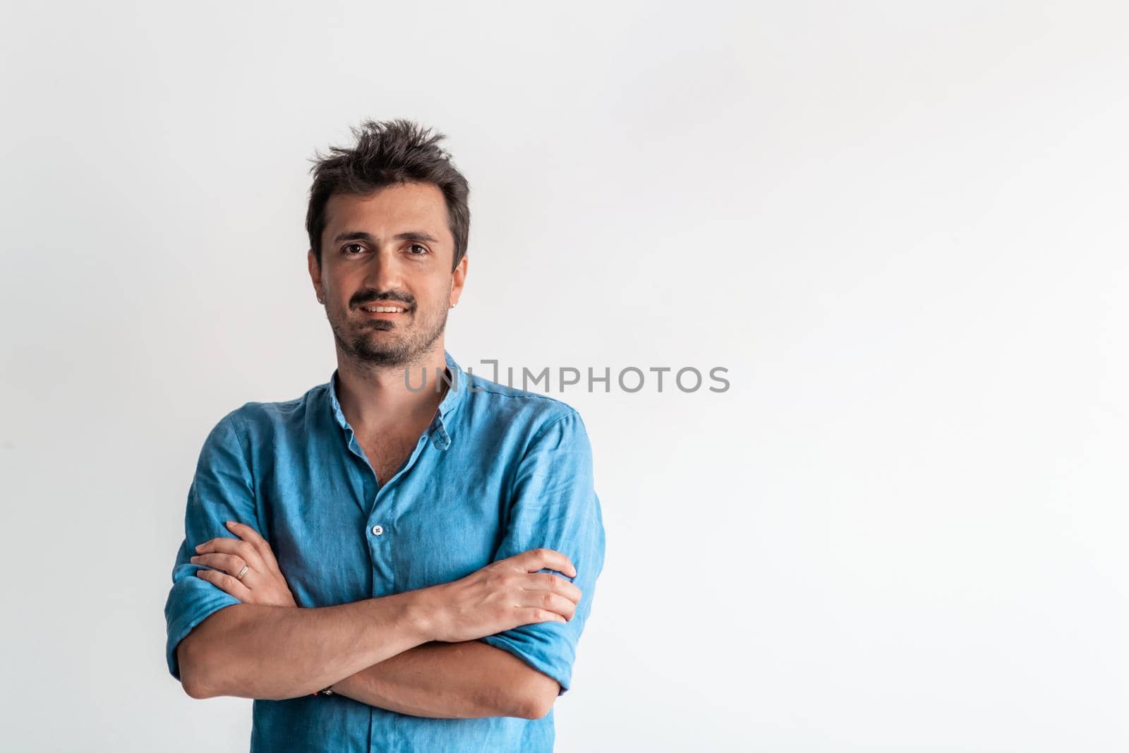 Formal business male portrait. A confident successful casual businessman or manager stands in front of a white background, arms crossed, looking directly at the camera and smiling friendly. High-quality photography.