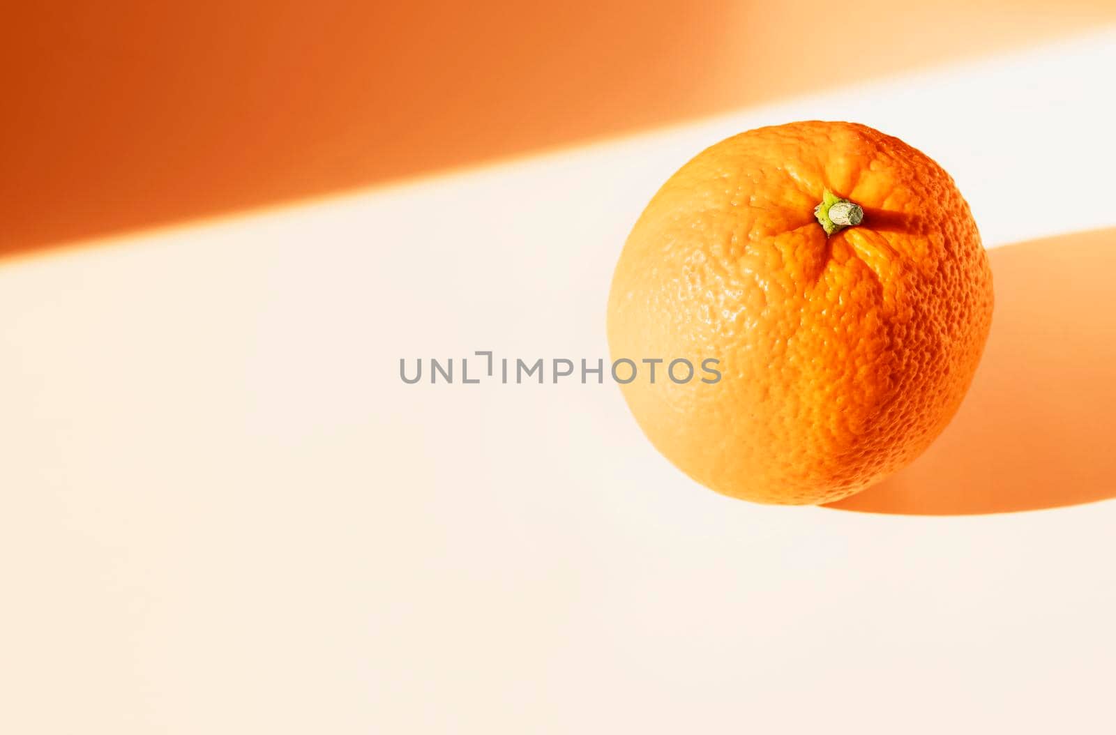 One orange fruit on white table , orange colored shadows , 