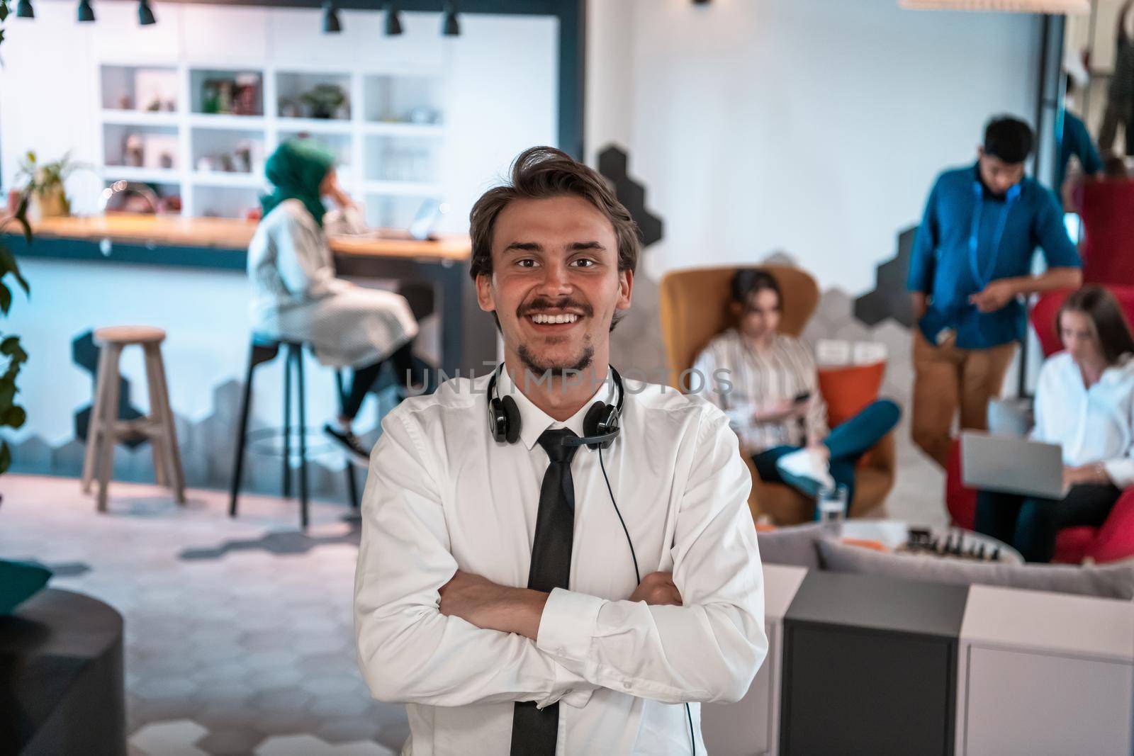 Portrait of successful businessman entrepreneur with headphones around his neck and colleagues in the background at busy startup office. High-quality photo
