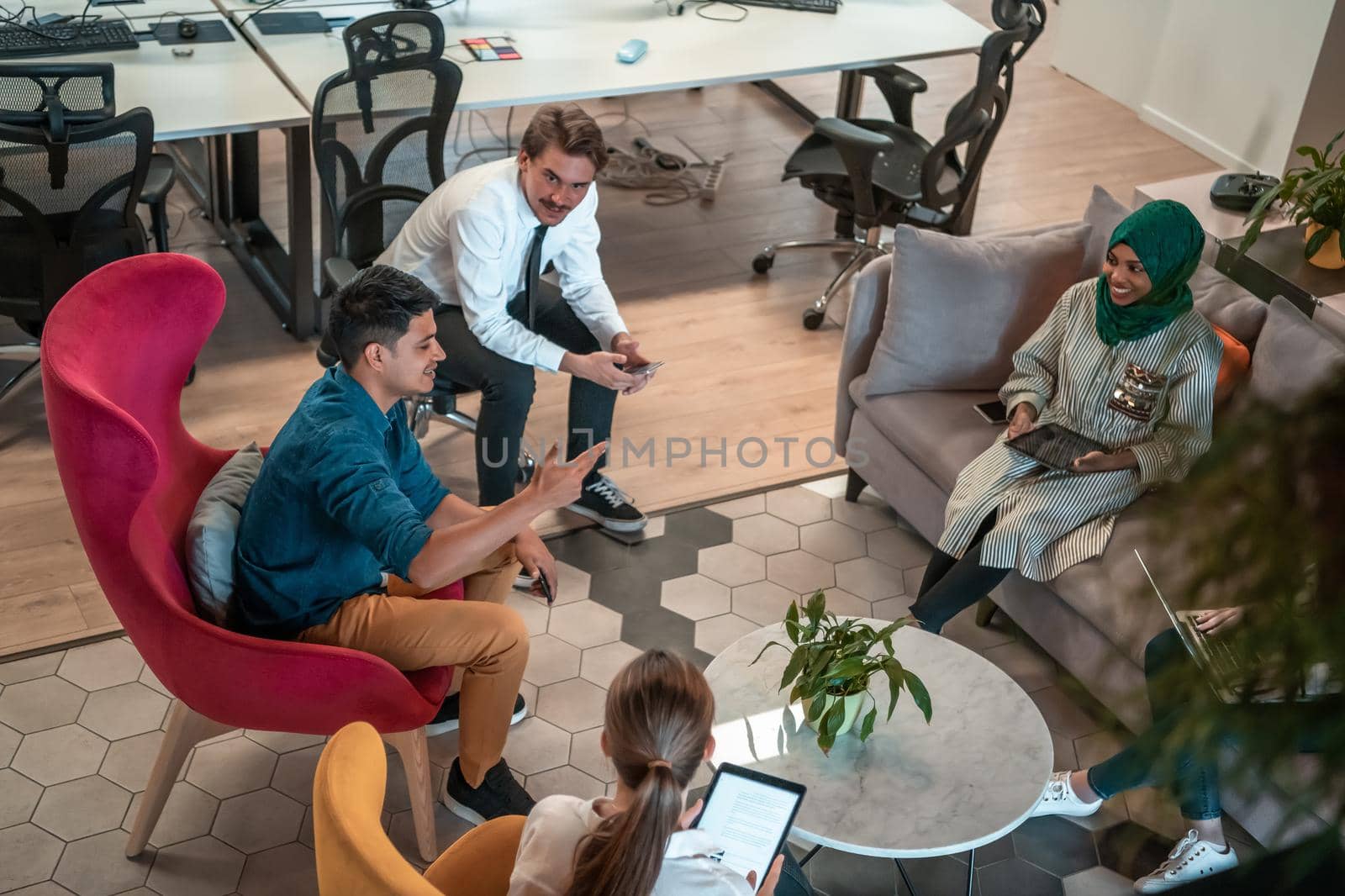 Multiethnic startup business team having brainstorming in relaxation area of modern office interior working on laptop and tablet computer. High-quality photo
